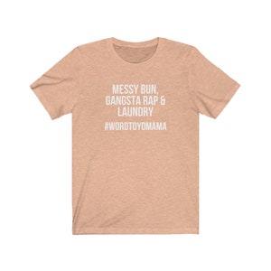K&ouml;nnte beinhalten: Ein pfirsichfarbenes T-Shirt mit dem wei&szlig;en Text "MESSY BUN, GANGSTA RAP & LAUNDRY" und dem Hashtag "#WORDTOYOMAMA". Das T-Shirt hat kurze &Auml;rmel und einen Rundhalsausschnitt.