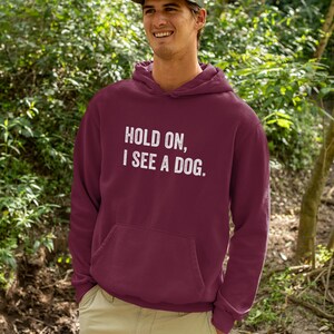 Pode incluir: Um moletom com capuz vinho com um gr&aacute;fico branco que diz "Hold on, I see a dog."