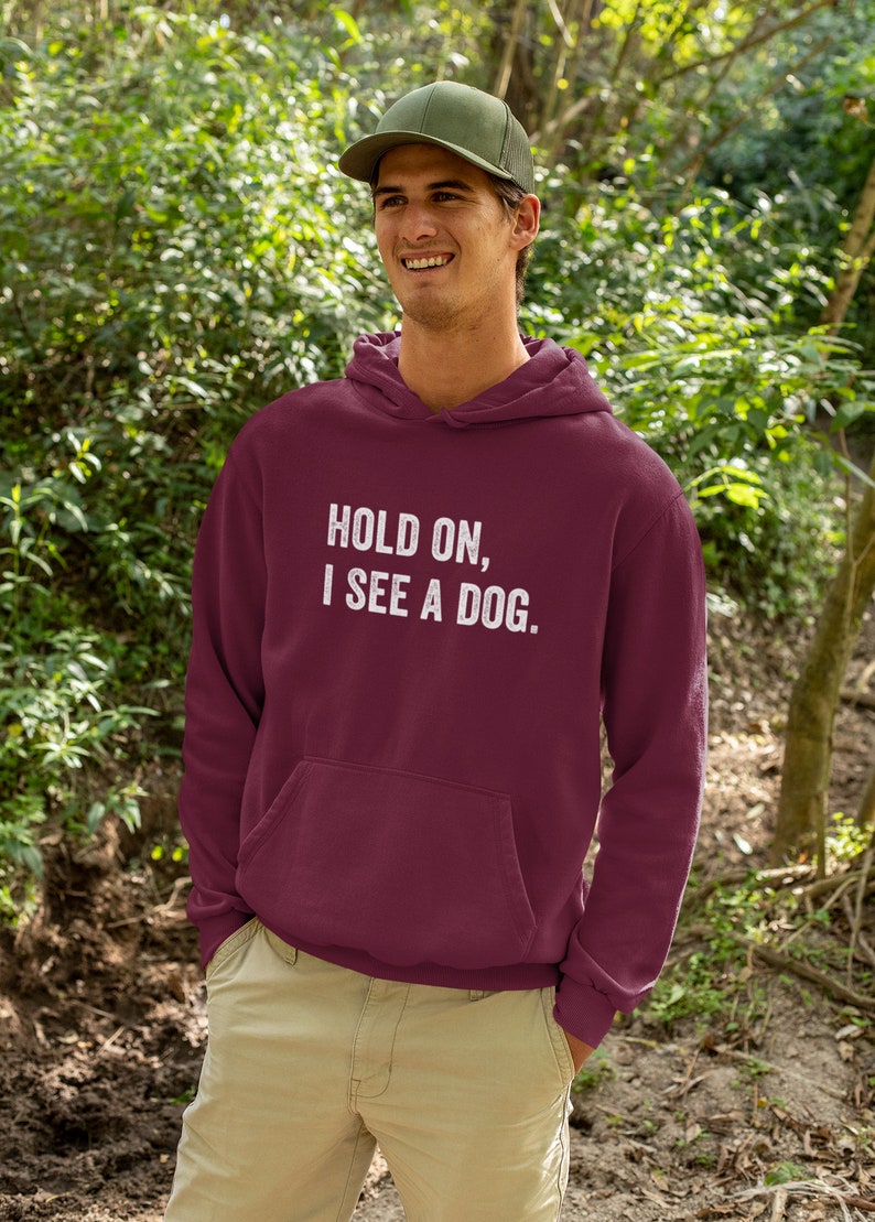 Pode incluir: Um moletom com capuz vinho com um gr&aacute;fico branco que diz "Hold on, I see a dog."