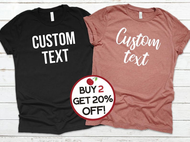 May include: Two t-shirts, one black and one dusty rose, each with the words "CUSTOM TEXT" printed in white. A circular graphic with a cherry and the text "BUY 2 GET 20% OFF!" is in the foreground.