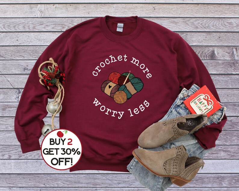 May include: A maroon sweatshirt with the text "crochet more worry less" and a graphic of yarn balls and a crochet hook. The text "BUY 2 GET 30% OFF!" is on a red circle sticker.
