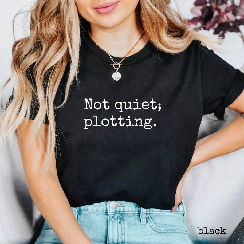 May include: Black crew neck t-shirt with the white text "Not quiet; plotting." printed on the front. The shirt is a solid black color and is made of a soft material. The word "black" is printed at the bottom right.