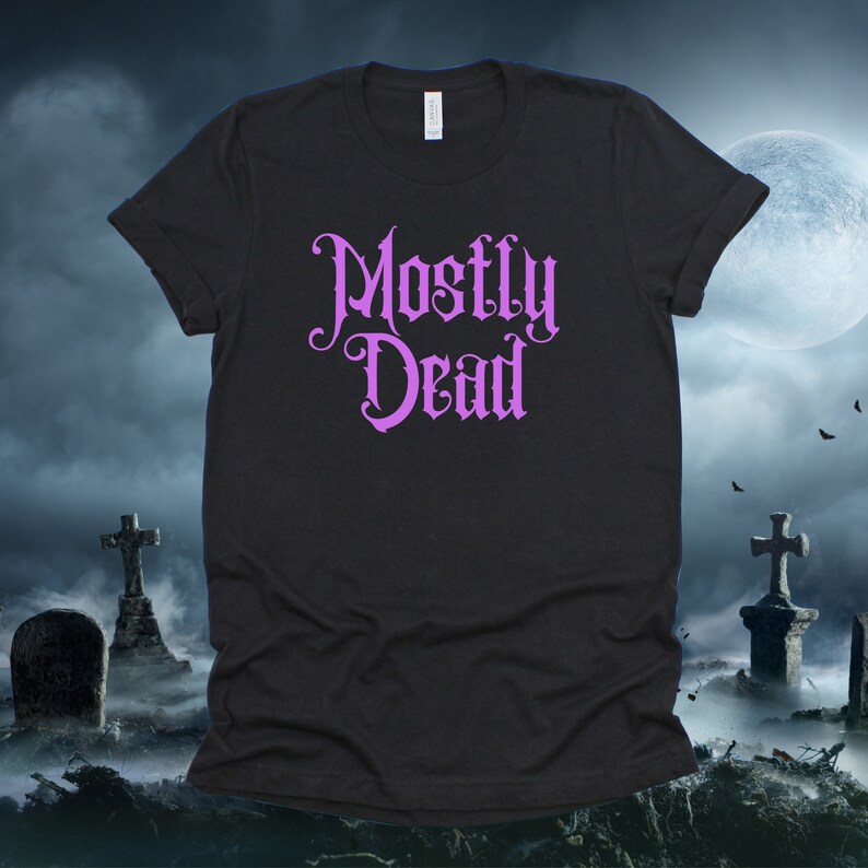 May include: Black t-shirt with a purple graphic that says "Mostly Dead" in a gothic font. The shirt is photographed against a dark background with a full moon and two crosses.