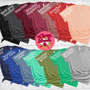 K&ouml;nnte beinhalten: Eine Auswahl an gefalteten T-Shirts in verschiedenen Farben, darunter Schwarz, Dunkelgrau-Melange, Bordeaux, Heather-Himbeere, Heather-Mauve, Heather-Rot und Heather-Pfirsich. Weitere Farben sind Heather-Navy, Heather-Royalblau, Heather-Schiefer, Heather-Minze, Heather-Gr&uuml;n, Heather-Kelly und Athletic-Heather. Ein Logo ist sichtbar.