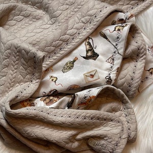 Könnte beinhalten: Eine beige gesteppte Babydecke mit einer weißen und braunen gemusterten Auskleidung. Die Decke ist gefaltet und liegt auf einem weißen Kunstfellteppich.