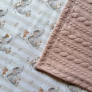Könnte beinhalten: Eine rosafarbene gesteppte Babydecke mit einem weißen und braunen Stoff mit einem sich wiederholenden Muster aus Elefanten und Mäusen. Der Stoff hat einen gestreiften Hintergrund mit braunen und weißen Streifen.