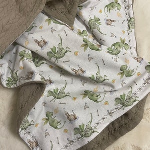 Könnte beinhalten: Eine weiche, braune Steppdecke mit einer weißen Baumwollfutter, die ein sich wiederholendes Muster aus grünen Drachen, Burgen und Schwertern zeigt.