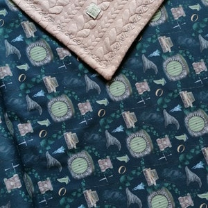 Könnte beinhalten: Ein zweiteiliges Textilset. Das obere Teil ist ein hellbrauner, gesteppter Stoff mit einem Blättermuster. Das untere Teil ist ein dunkelblauer Stoff mit einem sich wiederholenden Muster aus Hobbit-Tür-Illustrationen, Schwertern und anderen Fantasy-Elementen.