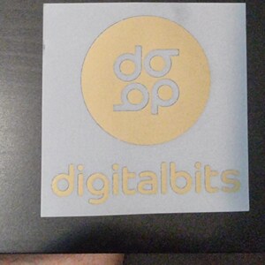 May include: A light blue square with a gold circle in the center. The circle contains the text "d&p" in a white font. Below the circle is the text "digitalbits" in a gold font.