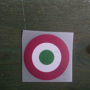 May include: A circular sticker featuring a target design with a solid green center, a white middle ring, and a dark pink outer ring. The sticker is on a square backing sheet with the text TY-168 printed vertically along the right side of the circle.