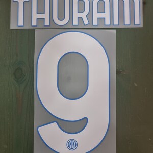 May include: White soccer jersey number with blue outline. The number is 9. The name "THURAM" is on the top of the jersey. The Inter Milan logo is below the number.