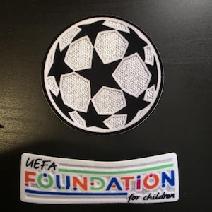 May include: A circular embroidered patch featuring a black and white soccer ball design with star patterns, alongside a rectangular white patch with the text UEFA FOUNDATION for children in blue, red, green, and orange lettering.
