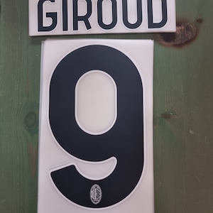 May include: White and black jersey number 9 with the name "GIROUD" on a separate white and black nameplate. The number has a small black and red logo in the bottom centre.