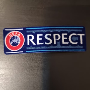 May include: A blue and white patch with the word "RESPECT" in white letters and a UEFA logo in the corner. The patch has a blue border with a light blue stripe.