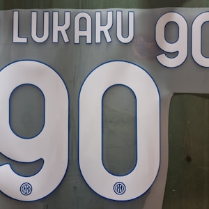 Könnte beinhalten: Weiße Trikotnummer mit blauem Umriss, mit dem Namen "LUKAKU" und der Nummer "90" mit einem kleinen Inter Mailand-Logo auf jeder Nummer.