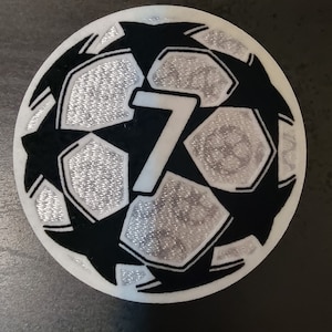 May include: A white and black football patch with the number 7 printed in white on the centre of the ball.