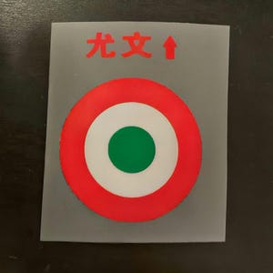 Può includere: Un bersaglio rosso, bianco e verde con una freccia che punta verso l'alto. Il testo "先攻" è scritto in rosso sopra il bersaglio.