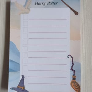 Peut inclure: Un bloc-notes blanc sur le thème d'Harry Potter. Le bloc-notes présente un hibou blanc, une baguette magique, un chapeau de sorcière et un balai. Le bloc-notes a une section lignée pour écrire.