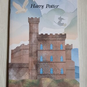 Peut inclure: Une illustration aquarelle d'un château brun avec des fenêtres bleues, un hibou blanc volant dans le ciel et le texte "Harry Potter".
