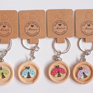 Peut inclure: Six porte-clés en bois avec des designs de coccinelles de différentes couleurs. Chaque porte-clés a une petite étiquette brune avec le texte "Je t'aime avec tout mon coeur - Merci".