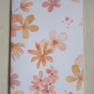 Peut inclure: Un carnet blanc avec un motif floral. Les fleurs sont dans des tons de rose et d'orange et sont peintes dans un style aquarelle.