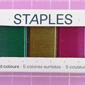Peut inclure: Une boîte d'agrafes avec le mot "STAPLES" imprimé sur le devant. La boîte contient 1000 agrafes de couleurs assorties : bleu, vert, or, rose et bleu. Le texte "5 couleurs assorties" est imprimé en bas.