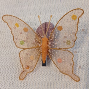 Peut inclure: Une pince à cheveux en forme de papillon délicate avec une conception d'aile transparente et transparente. Les ailes sont ornées de petites fleurs de couleur pastel et de perles nacrées. La pince est de couleur brun clair et possède un fermoir en métal.