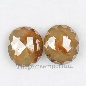 May include: Two round, faceted, brown diamonds in a white box. Thegemsemporium is printed on the bottom of the box.