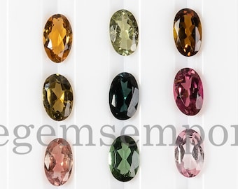 May include: Assortment of oval-shaped gemstones in various colors, including green, pink, brown, and black. The gemstones are arranged in rows on a white background. Thegemsemporium is written in black text at the bottom of the image.