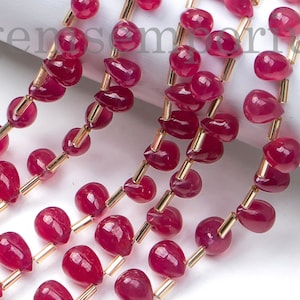 May include: Close-up of multiple strands of ruby red teardrop-shaped beads. The beads are strung on gold-coloured wire, with a tassel at the top. The beads are a deep, rich red colour, and the gold wire adds a touch of elegance.