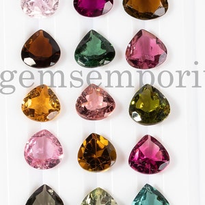 May include: Assortment of 18 faceted, pear-shaped gemstones in various colors, including pink, green, brown, and yellow. The gemstones are arranged in three rows of six, on a white background. Thegemsemporium is printed in black text at the top of the image.