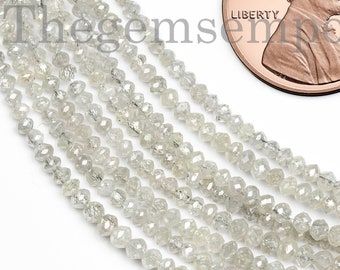 May include: A strand of white diamond beads, approximately 2mm in size, with a faceted, rough cut. The beads are strung on a clear thread and are shown next to a US penny for scale.