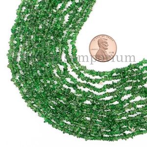 Puede incluir: Una hebra de chips de piedras preciosas verdes, aproximadamente 100 piezas, con un centavo de dólar estadounidense para la escala. Las chips son de forma irregular y tienen una textura rugosa y natural.