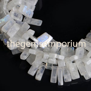 May include: A strand of white moonstone beads, each bead is a rectangular prism with a iridescent sheen. The beads are arranged in a loose, flowing pattern.