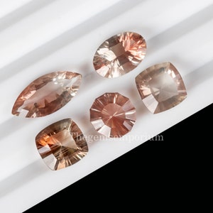 May include: Five faceted sunstone gemstones in various shapes and sizes. The gemstones are a light peach color with a slight shimmer. The gemstones are arranged on a white surface.