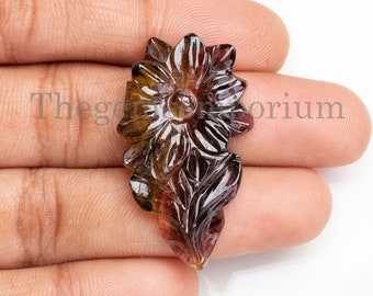 May include: A carved flower pendant made from a brown and black gemstone. The flower has a detailed design with multiple petals and leaves.