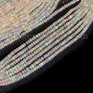 May include: A strand of white opal beads with iridescent rainbow colors. The beads are faceted and have a square shape. The beads are strung on a clear thread and are approximately 4mm in size.