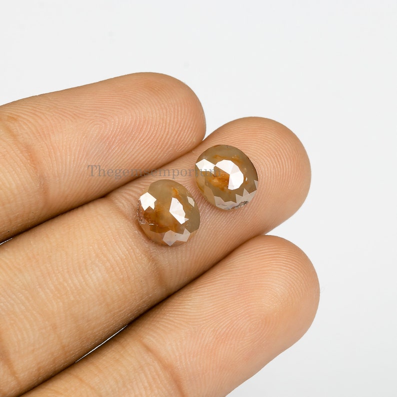 May include: Two brown rough diamonds with a faceted cut. The diamonds are held in a hand.