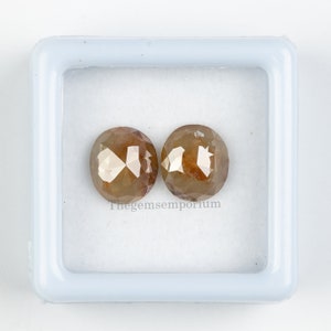 May include: Two brown, round, faceted diamonds in a white box. Thegemsemporium is printed on the bottom of the box.