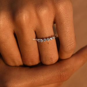 Puede incluir: Un anillo de plata con una fila de pequeñas piedras preciosas transparentes engastadas en una banda curva.