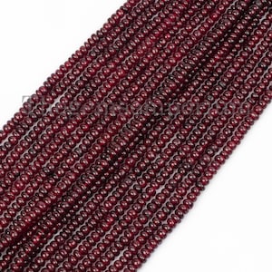 Könnte beinhalten: Eine Strähne tief roter Edelsteinperlen. Die Perlen sind rund und haben eine leicht facettierte Oberfläche. Die Perlen sind auf einem durchsichtigen Faden aufgefädelt.