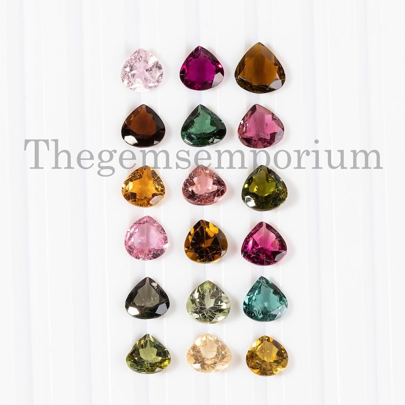 May include: Assortment of 18 faceted, pear-shaped gemstones in various colors, including pink, green, brown, and yellow. The gemstones are arranged in three rows of six, on a white background. Thegemsemporium is printed in black text at the top of the image.