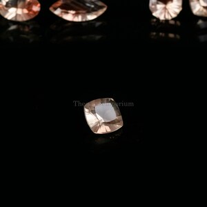 May include: A light pink square-shaped gemstone with a faceted cut. The gemstone is on a black background.
