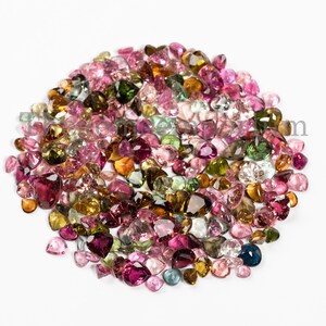 May include: A large collection of colorful gemstones in various shades of pink, green, brown, and yellow. The gemstones are all heart-shaped and are arranged in a loose pile.