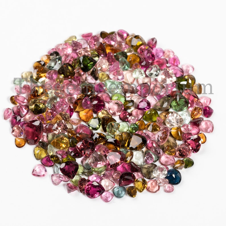May include: A large collection of colorful gemstones in various shades of pink, green, brown, and yellow. The gemstones are all heart-shaped and are arranged in a loose pile.