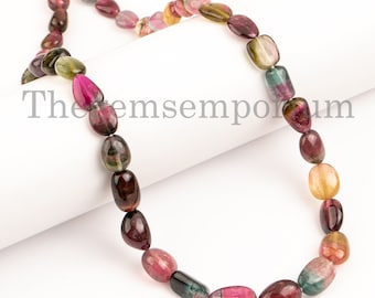 Könnte beinhalten: Eine Kette aus mehrfarbigen, ovalen Edelsteinperlen. Die Perlen sind eine Mischung aus Rosa, Grün und Braun. Die Perlen sind auf einer weißen Schnur aufgefädelt. Der Text "Thegemsemporium" ist im Hintergrund sichtbar.