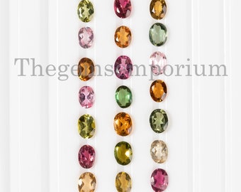 May include: An assortment of oval-cut gemstones in various colors, including pink, green, yellow, and brown, are arranged on a white surface. The gemstones are displayed in vertical rows, showcasing their polished surfaces and natural hues. The text "Thegemsemporium" is visible.