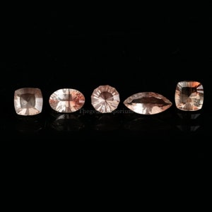 May include: Five faceted gemstones in various shapes and sizes, including square, oval, and marquise, with a light pink hue. The gemstones are arranged in a row on a black background.