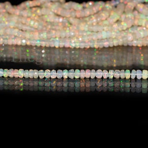 May include: A strand of white opal beads with iridescent flashes of color. The beads are faceted and have a rectangular shape. The beads are strung on a clear thread and are lying on a black surface.