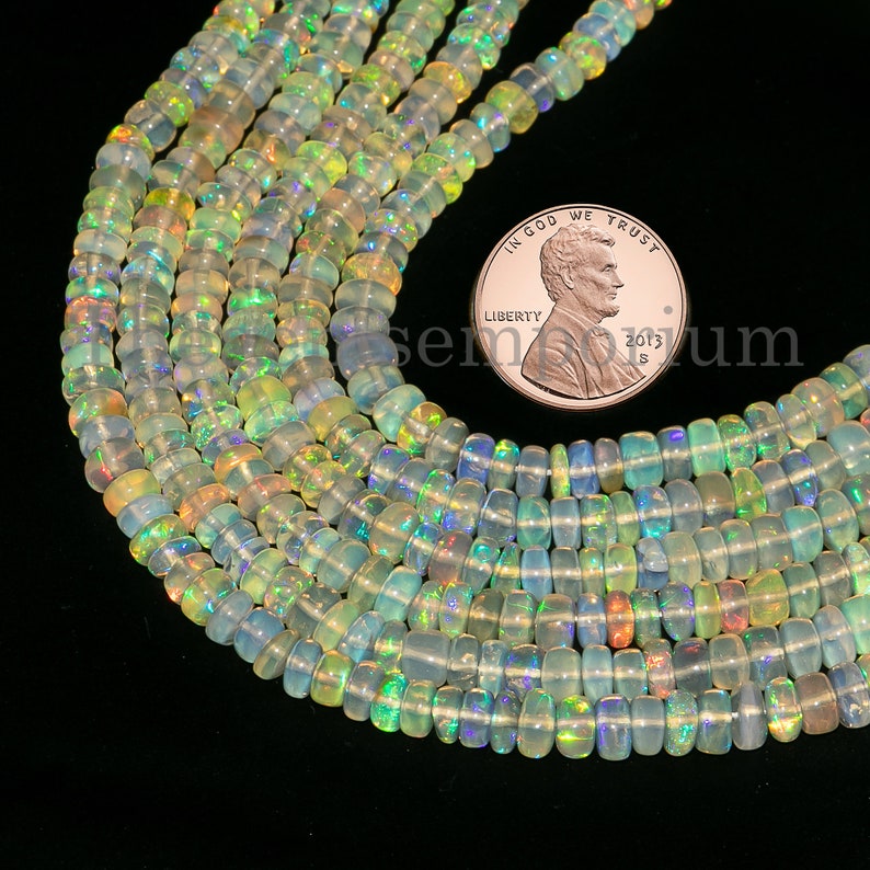 Puede incluir: Una hebra de cuentas de &oacute;palo iridiscente, de aproximadamente 4 mm de di&aacute;metro, con una variedad de colores que incluyen verde, azul y amarillo. Las cuentas est&aacute;n enhebradas en un hilo transparente y se muestran junto a un centavo estadounidense para la escala.
